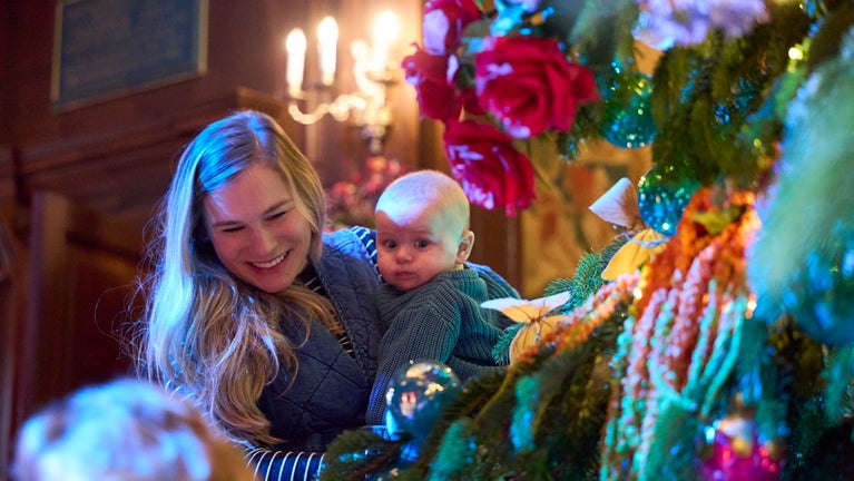 Alice's Christmas in Wonderland at Polesden Lacey 2025 - a mother holding a young baby smiles at a decorated Christmas tree